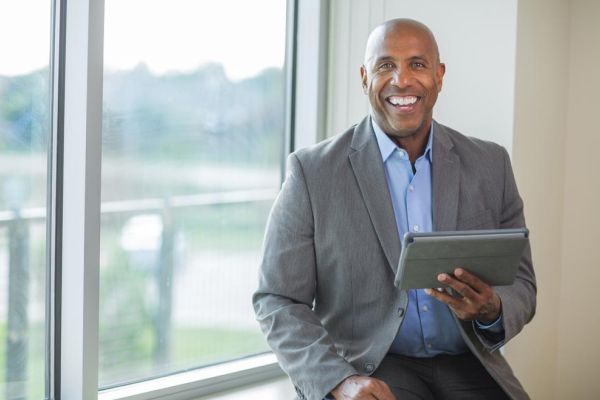 smiling businessman holding tablet in front of office window